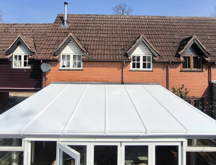 An insulated panel conservatory roof in white composite panels on a white framed conservatory, seen from the garden against a brick house.