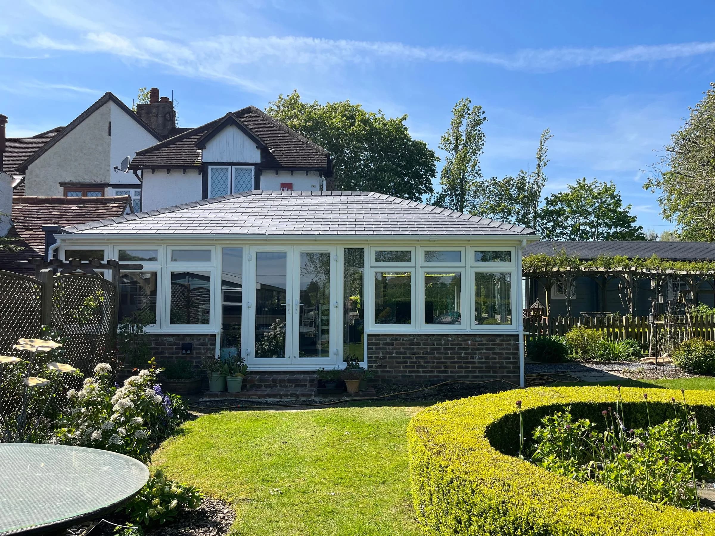 A conservatory with a SupaLite lightweight tiled roof in grey slate-effect tiles, white frames and a pair of French doors, seen across the lawn.